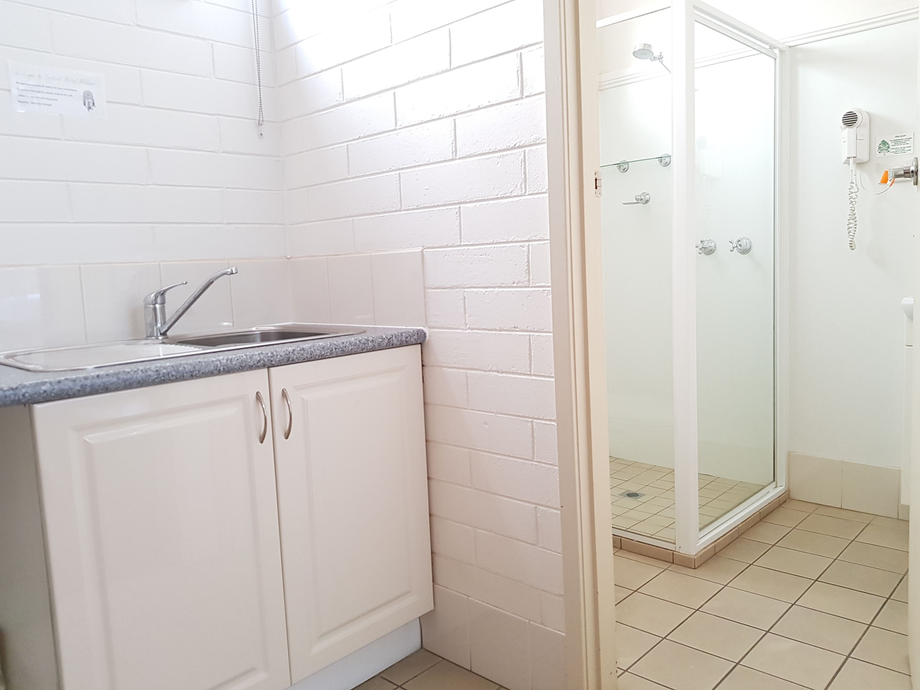 Un baño con paredes de azulejos blancos, cabina de ducha de vidrio y lavamanos con encimera de granito.