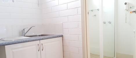 Un baño con paredes de azulejos blancos, cabina de ducha de vidrio y lavamanos con encimera de granito.