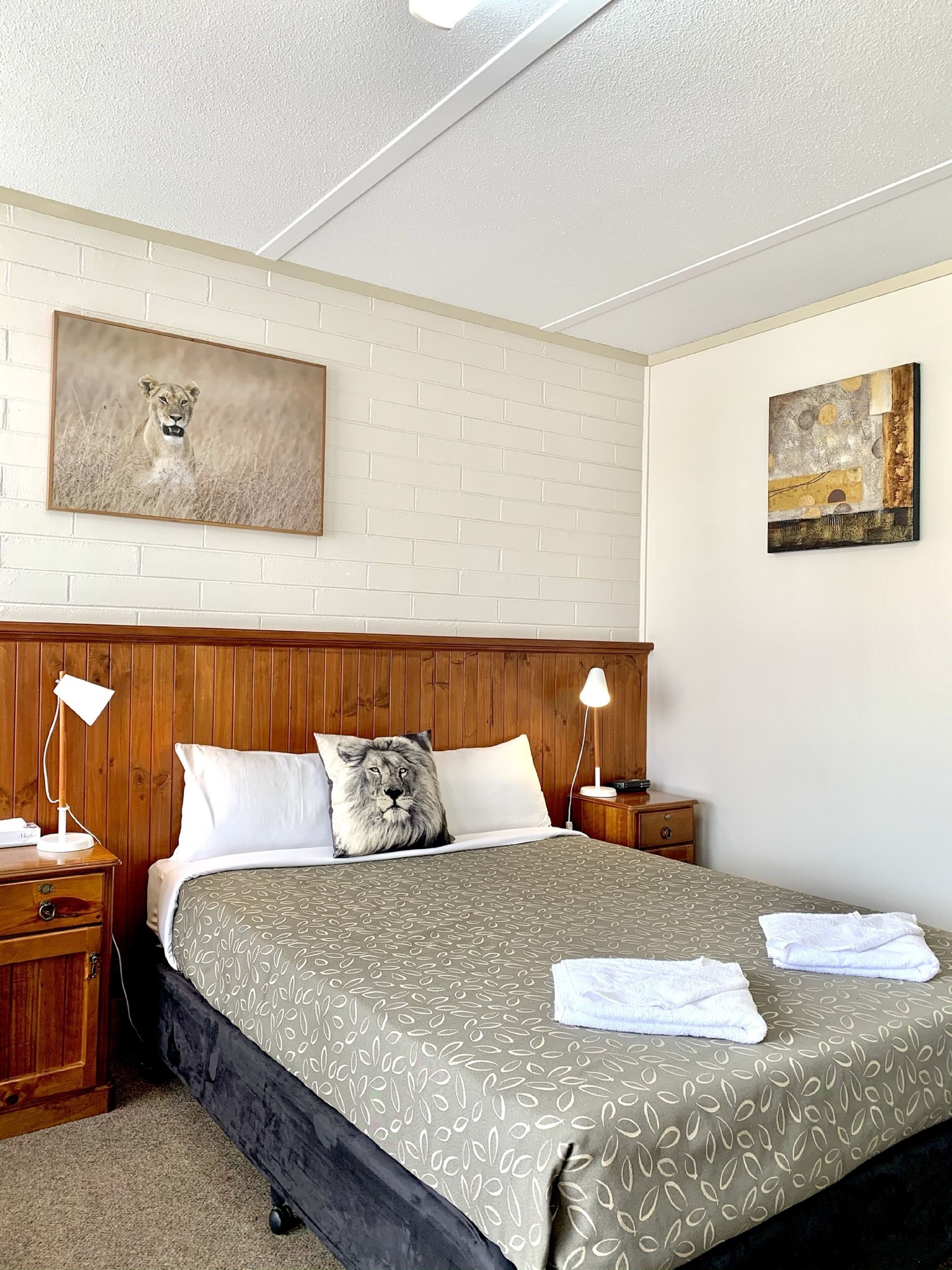 A hotel room with a brick-patterned wall, a bed with a patterned bedspread, two bedside tables with lamps, and two paintings.