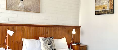 A hotel room with a brick-patterned wall, a bed with a patterned bedspread, two bedside tables with lamps, and two paintings.