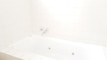 Eine weiße Badewanne mit zwei Wasserhähnen und einem Abfluss.
