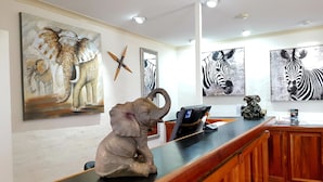 Un mostrador de recepción con acabado de madera, encimera negra y una escultura decorativa de elefante. Hay obras de arte enmarcadas de elefantes y cebras en la pared.