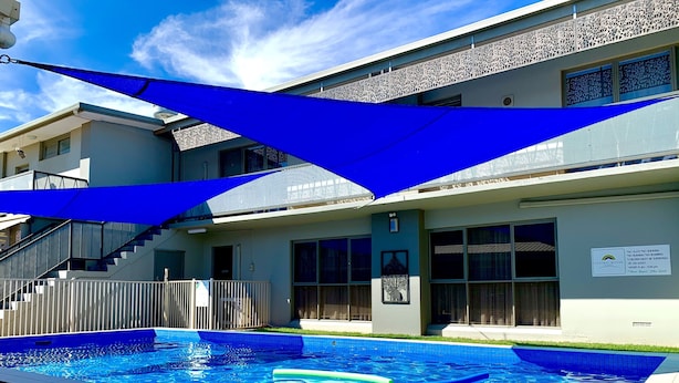 Un hotel moderno con piscina, un área exterior techada y una escalera que conduce a la entrada.
