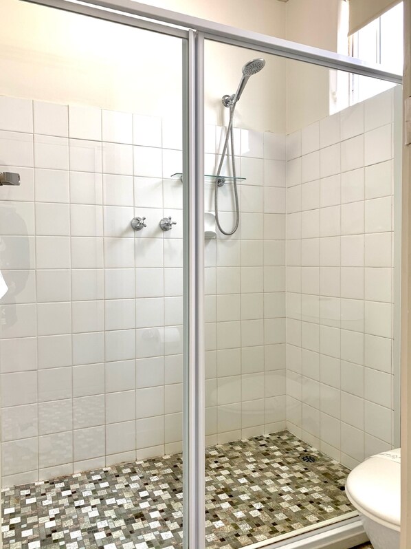 A glass-enclosed shower with white tiled walls and a checkered floor.