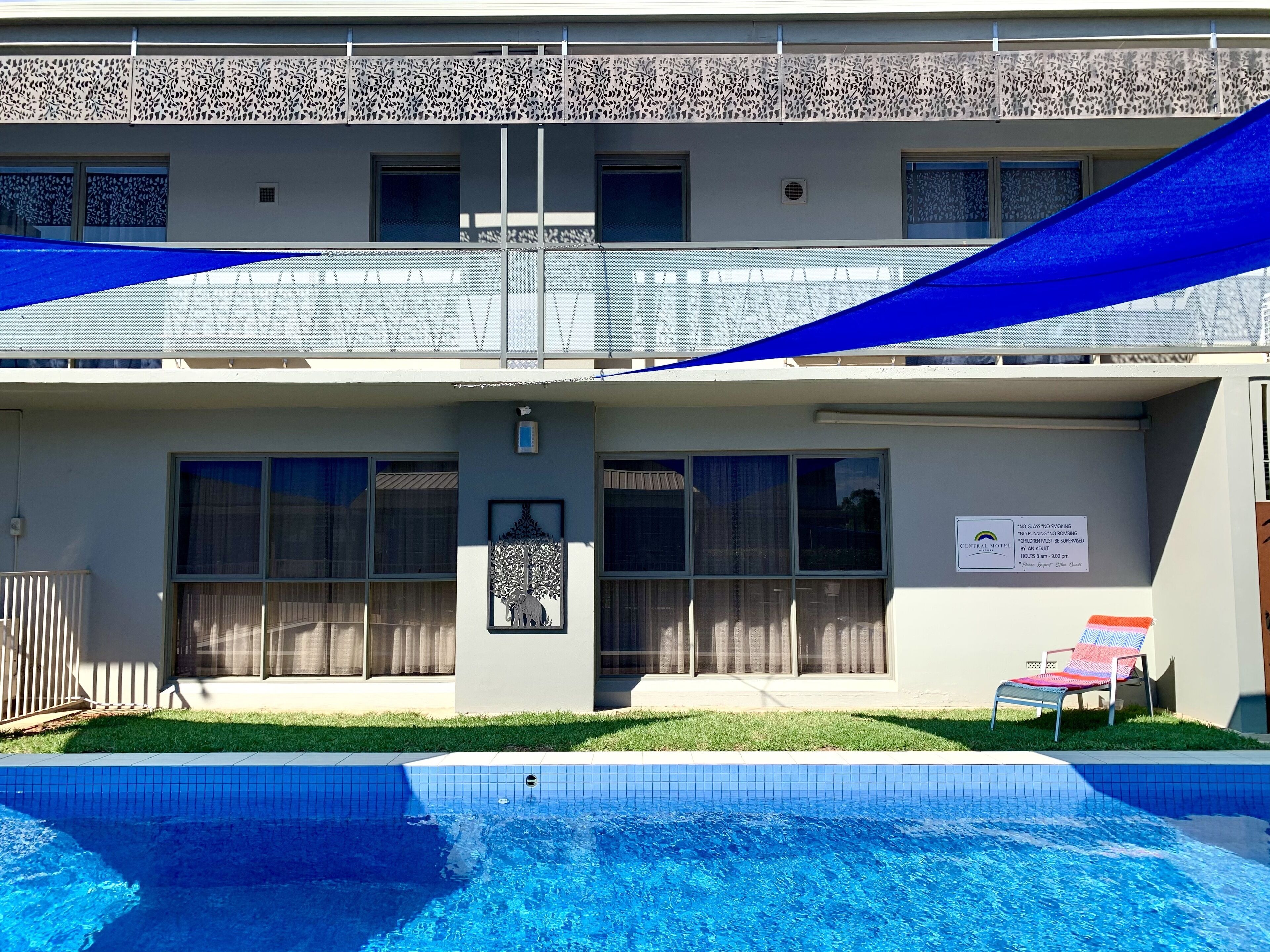 Um hotel com piscina, estrutura em dois andares e placa indicando proibição de estacionamento para veículos com vidro.