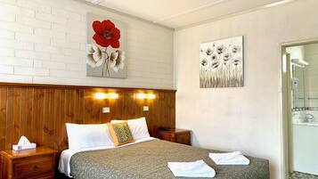 Une chambre d’hôtel avec une tête de lit en bois, deux lampes de chevet, un lit recouvert d’une couvre-lit à motifs et deux tableaux accrochés au mur.