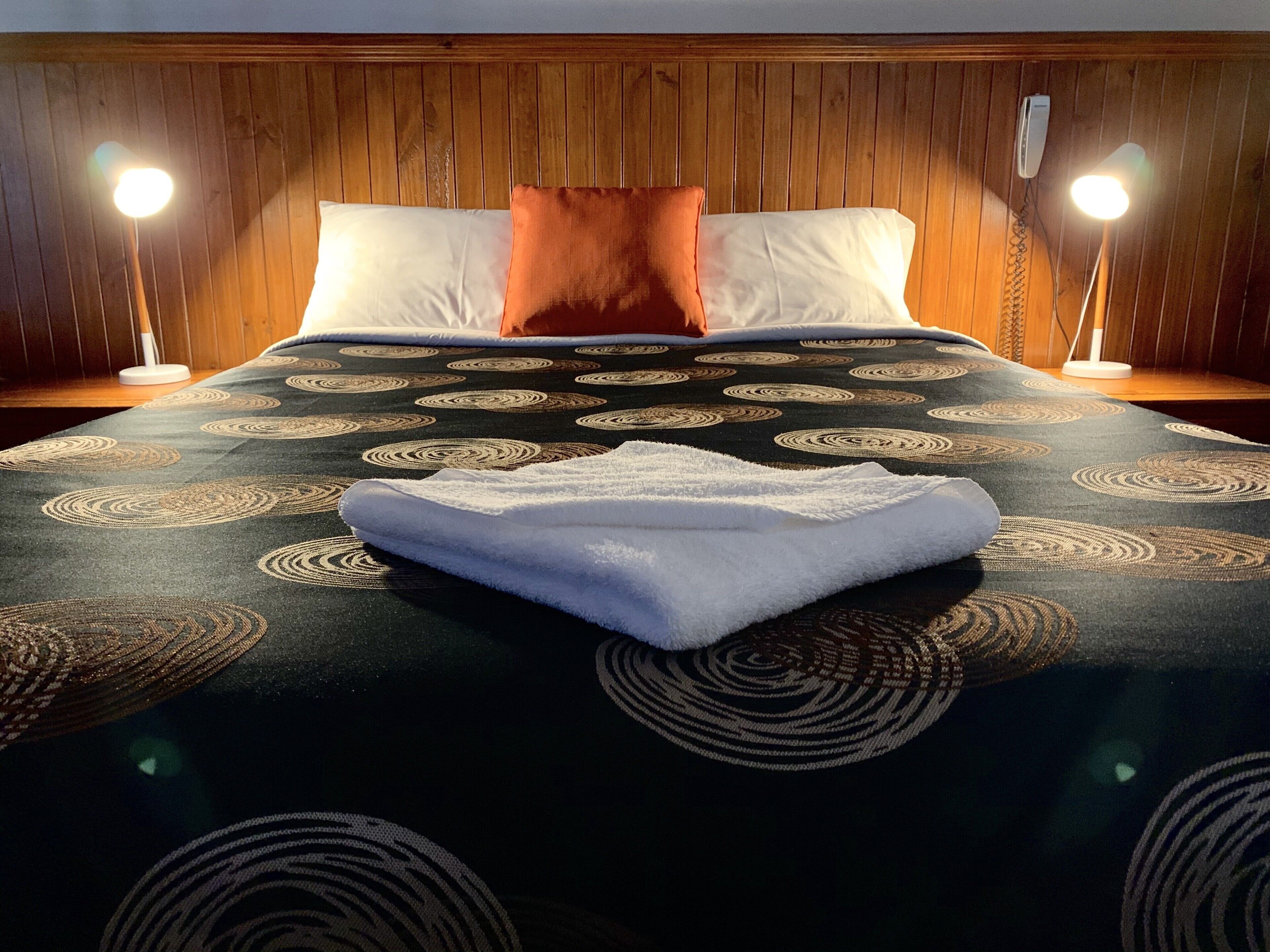 Una cama bien hecha con una colcha estampada, dos lámparas de noche y un cabecero de madera.