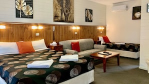 Habitación de hotel con una cama grande, dos sofás, un cabecero de madera y obras de arte en la pared.