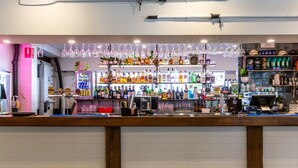 Una zona de bar con estantes llenos de botellas de licores, una caja registradora y copas colgando.