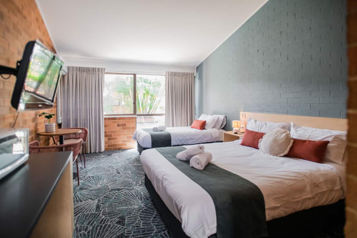 Habitación de hotel con dos camas, televisión, escritorio y ventana con cortinas.