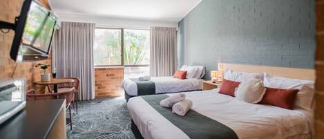 A hotel room with two beds, a TV, a desk, and a window with curtains.