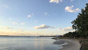 Una playa con aguas tranquilas, barcos y cielo despejado.