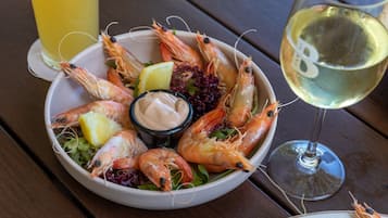 Un plato de camarones cocidos con rodajas de limón, un tazón pequeño de salsa y una copa de vino blanco sobre una mesa de madera.