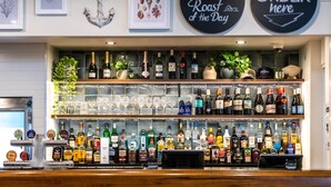 Zona de bar con estantes llenos de botellas de licores, vasos y un letrero que indica ordenar aquí.