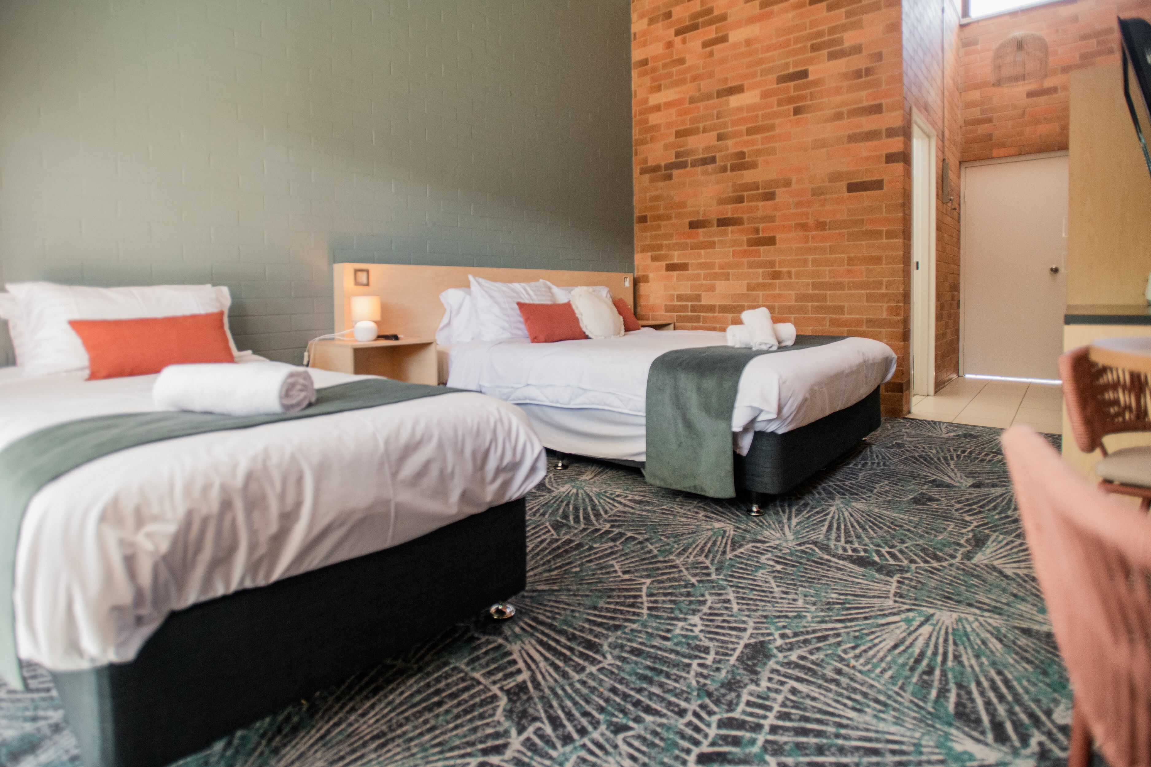 Una habitación de hotel con dos camas, una pared de ladrillo, una alfombra estampada y una puerta de madera.