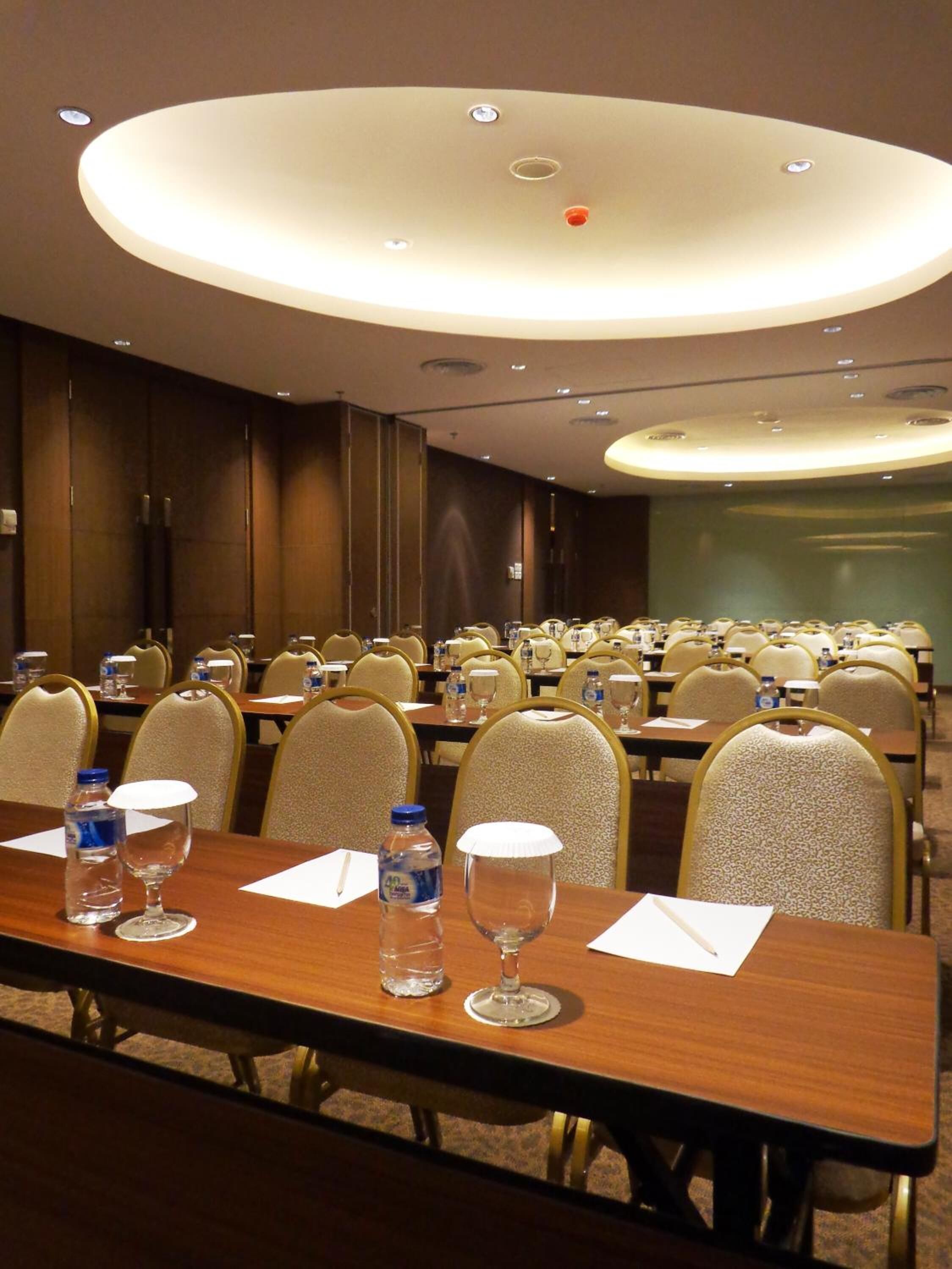 A conference room with multiple tables, chairs, and a large circular ceiling light fixture.
