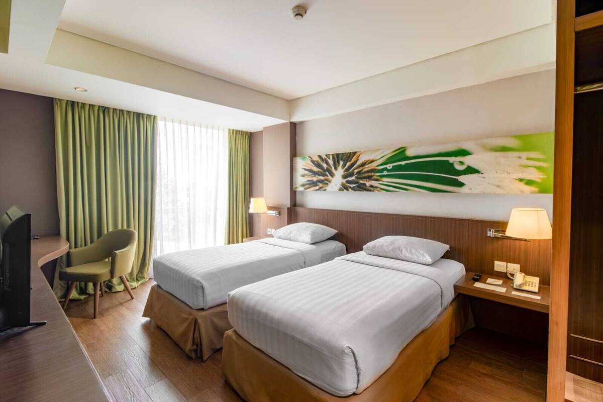 A hotel room with two beds, a desk, a chair, and a TV.