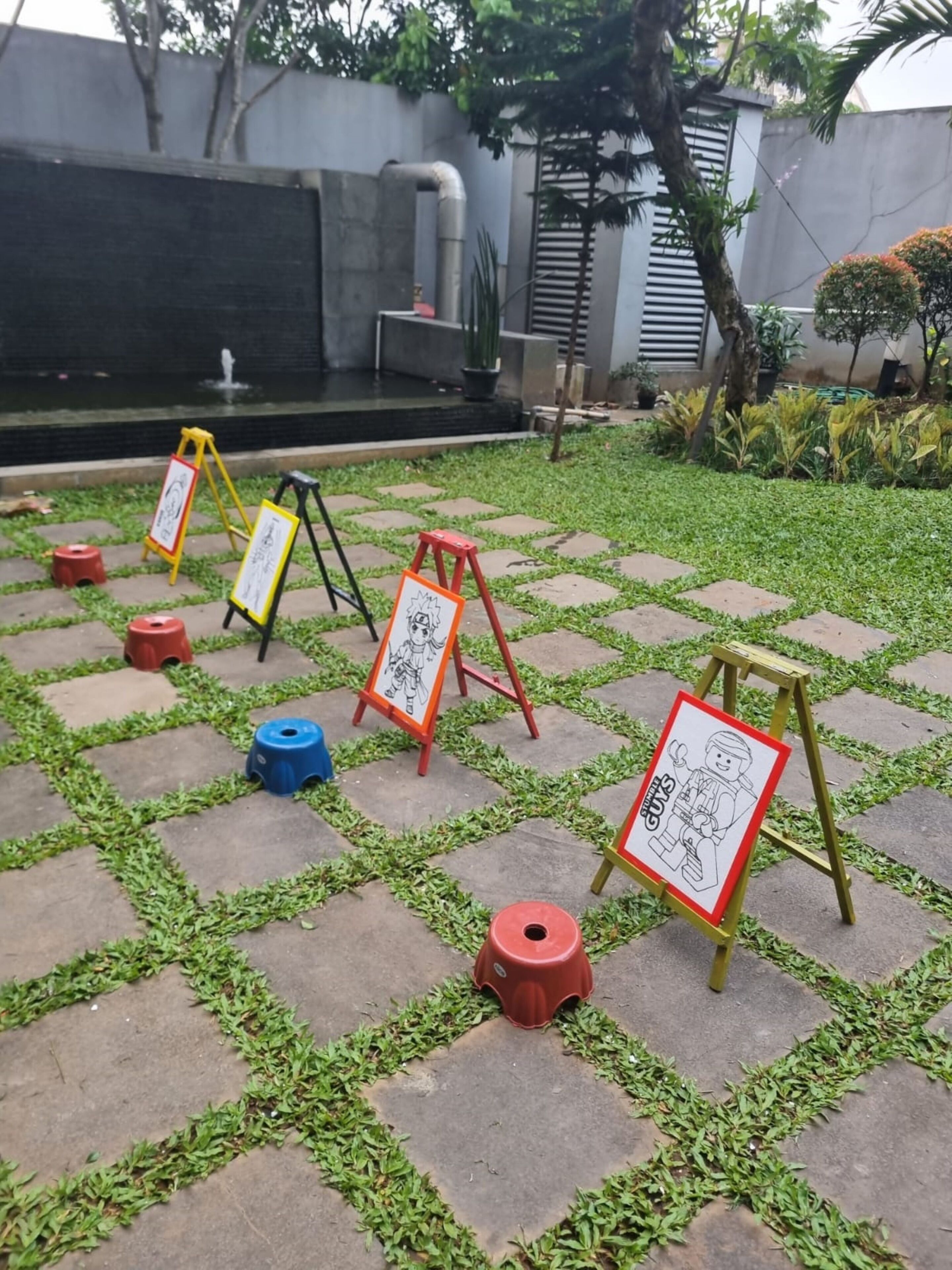 Un patio con una fuente, pavimentado con losetas de piedra, rodeado de vegetación y pequeños taburetes.