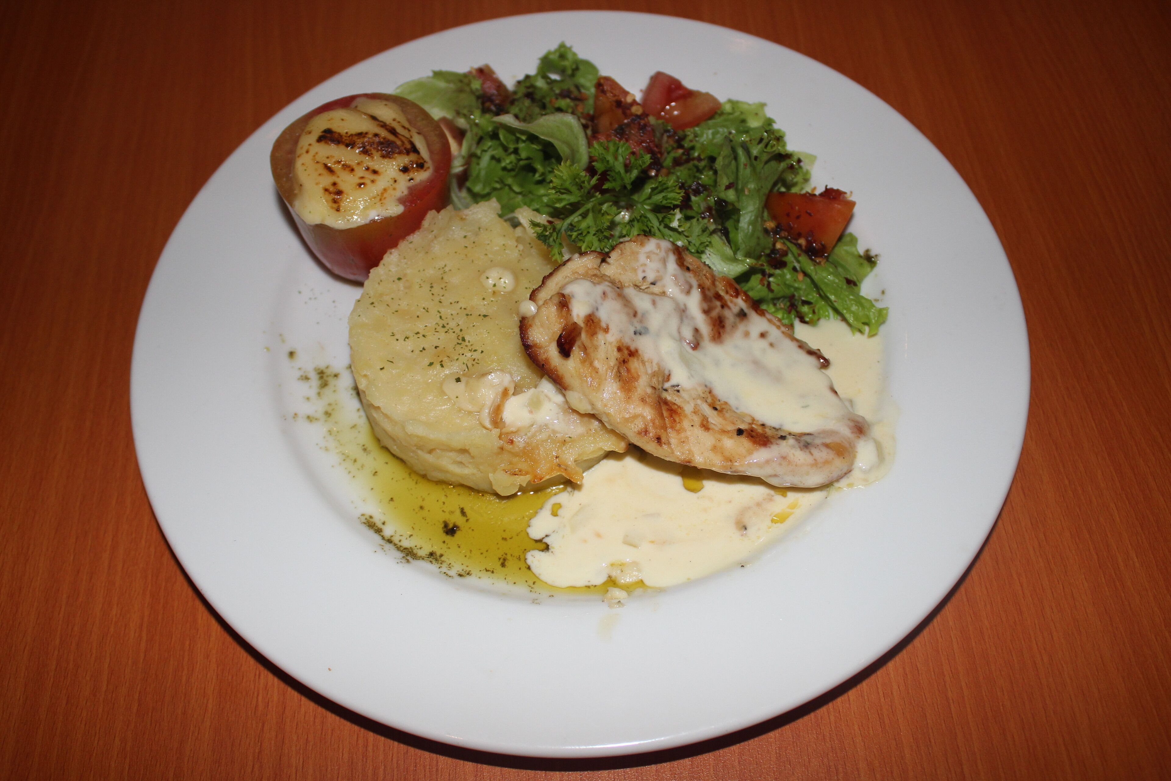 A plate with grilled chicken, mashed potatoes, a baked tomato, and a side salad.