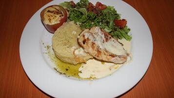 Un plato con pollo a la parrilla, puré de papas, tomate al horno y ensalada.