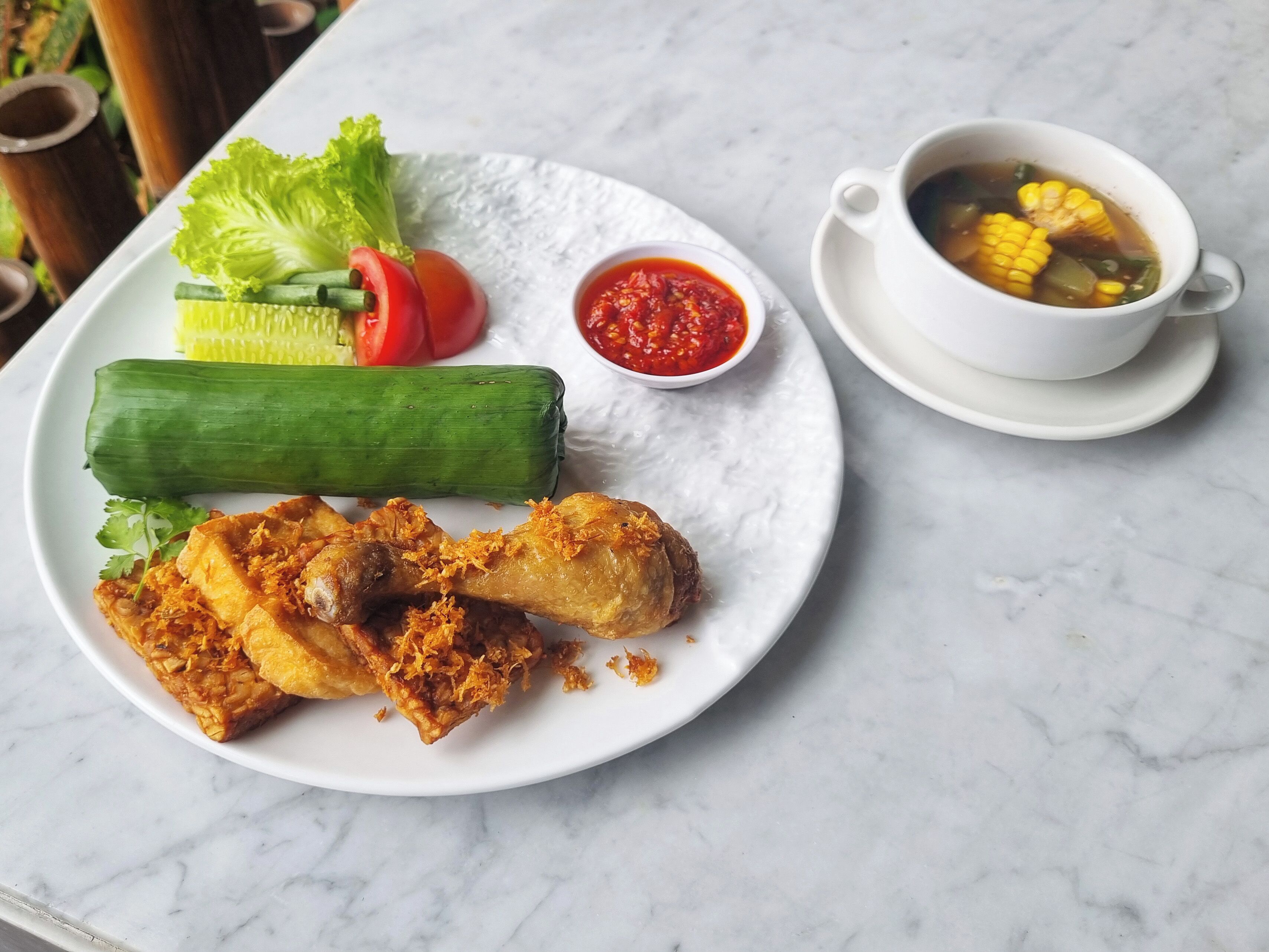 Un plato con pollo frito, verduras y una taza de sopa.