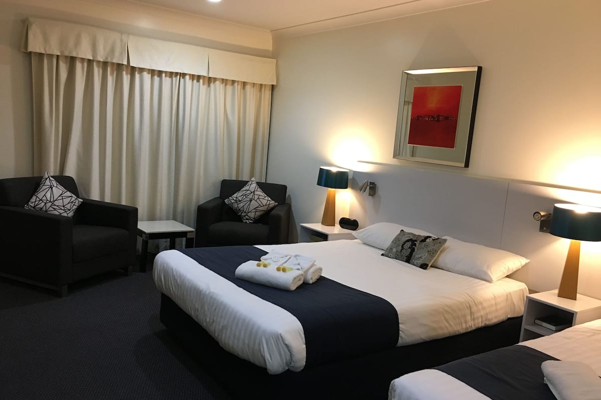 A hotel room with a large bed, two armchairs, a small table, and a nightstand with lamps.