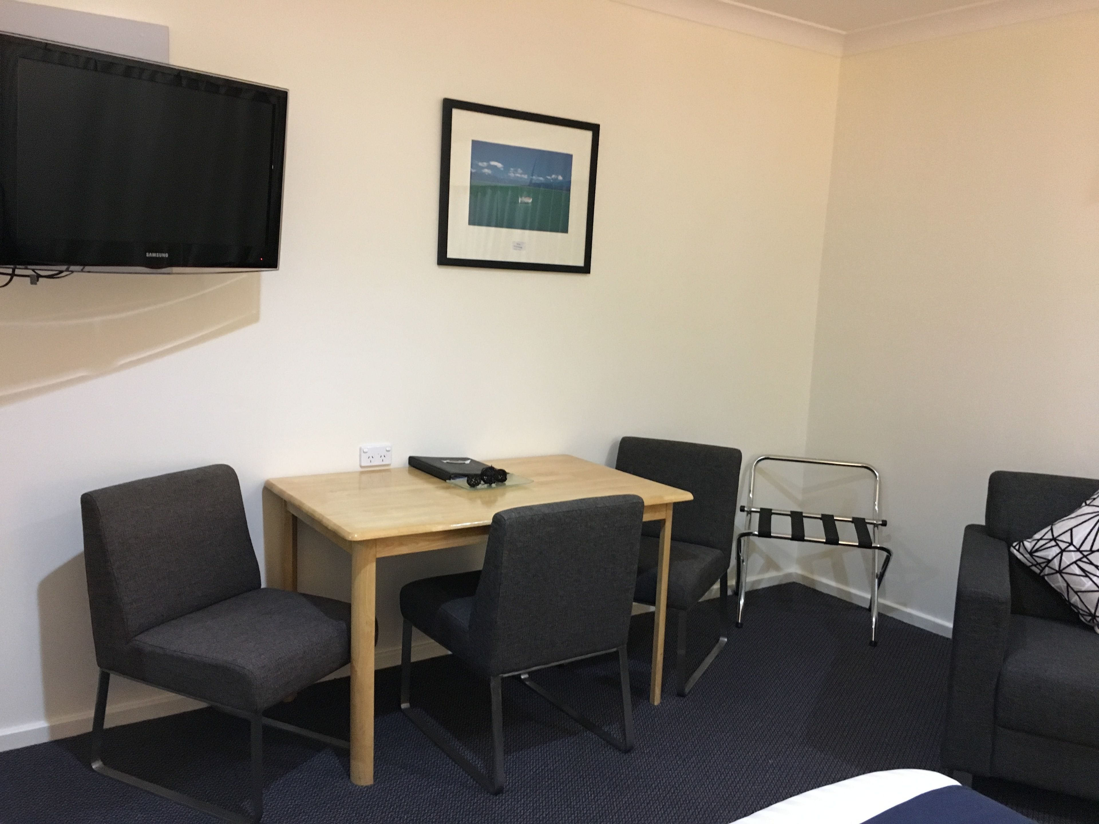 A compact hotel room with a bed, a desk with two chairs, a TV, and a framed picture on the wall.