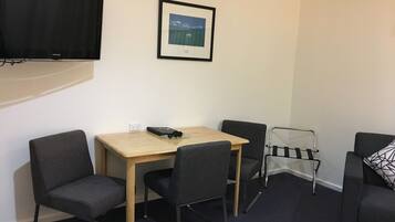 A compact hotel room with a bed, a desk with two chairs, a TV, and a framed picture on the wall.