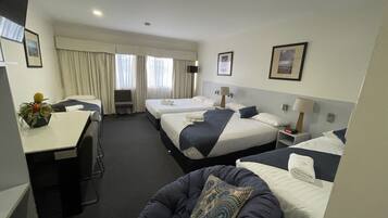A hotel room with two beds, a desk, a chair, and a small table with a plant.