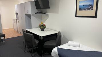 A hotel room with a bed, a desk with a chair, a television, a small table with a flower arrangement, and a framed picture on the wall.