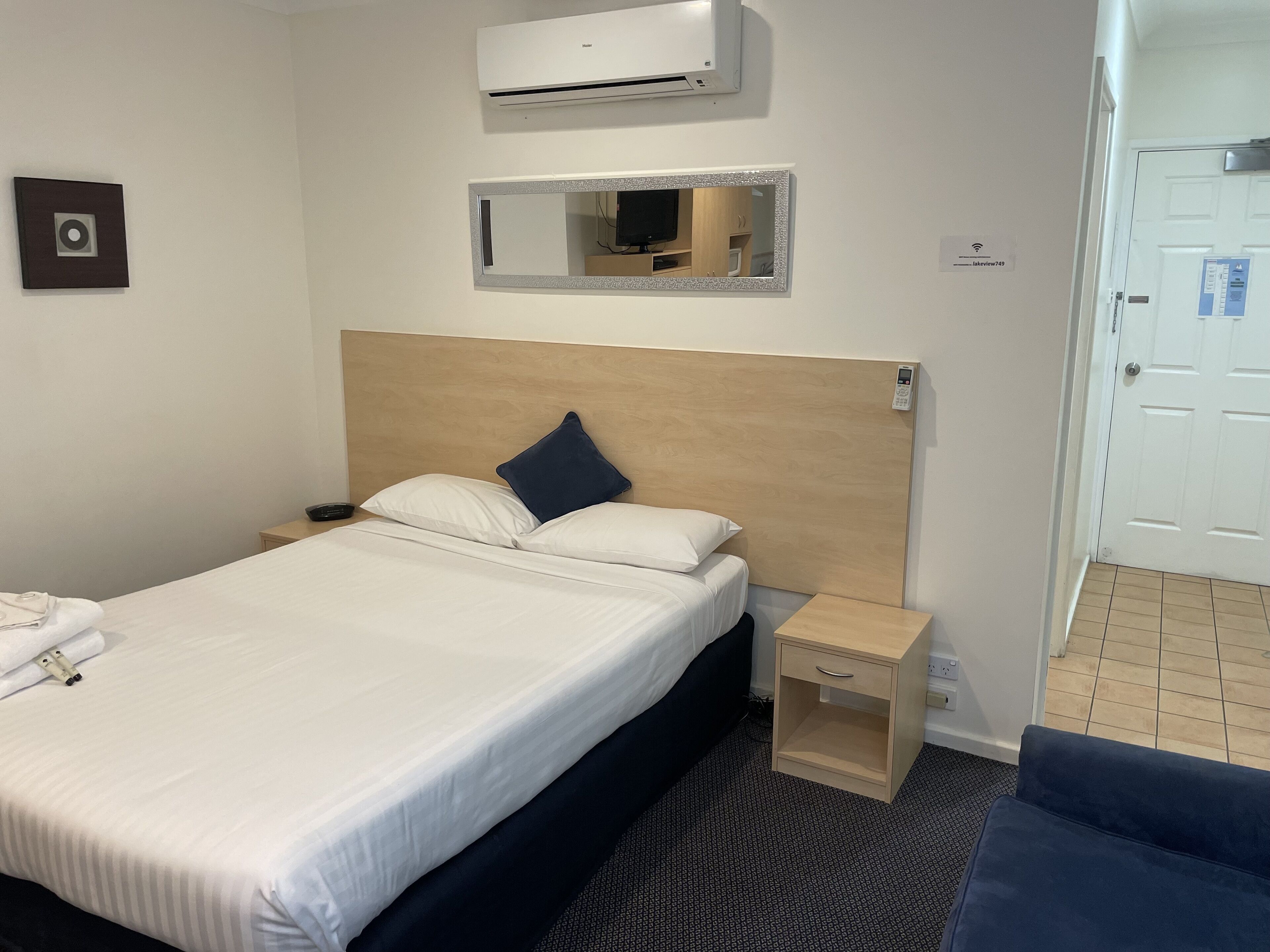Una habitación de hotel con una cama, mesita de noche y un aire acondicionado instalado en la pared.