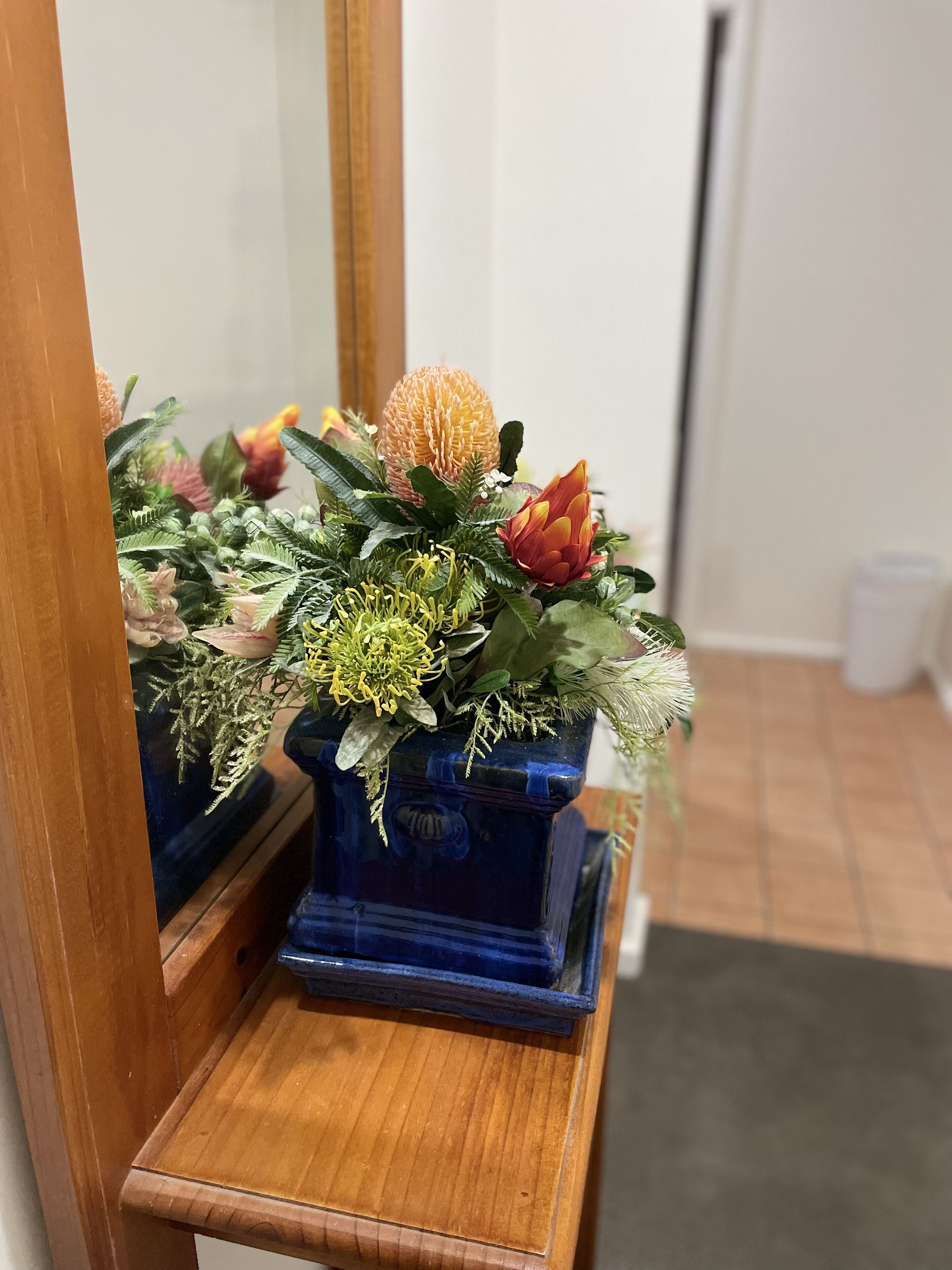 A blue vase with a floral arrangement on a wooden shelf.
