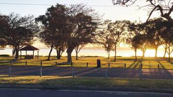 A park with a gazebo, trees, and a body of water during sunset.