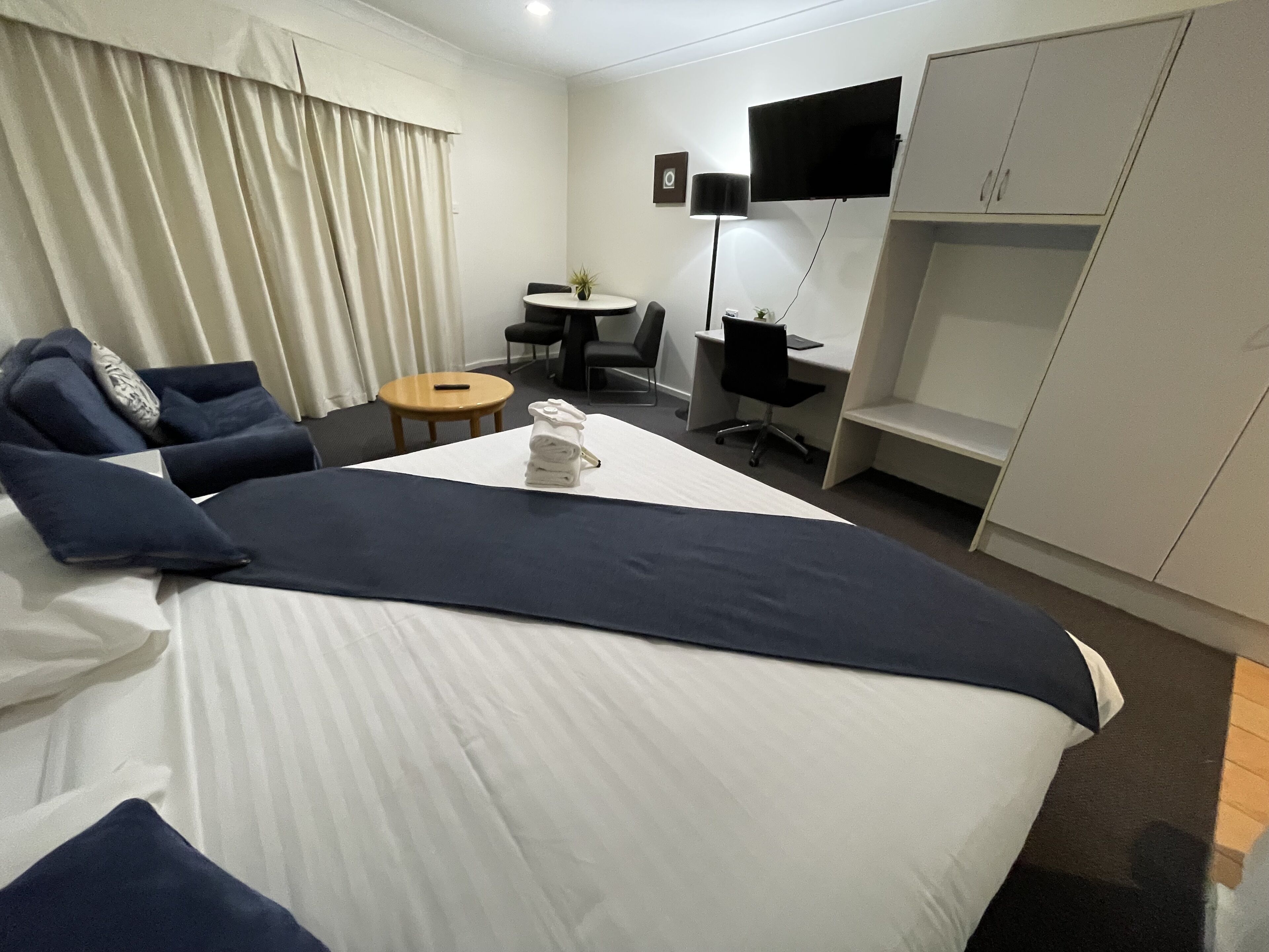Una habitación de hotel con cama, escritorio, silla, televisor y armario.