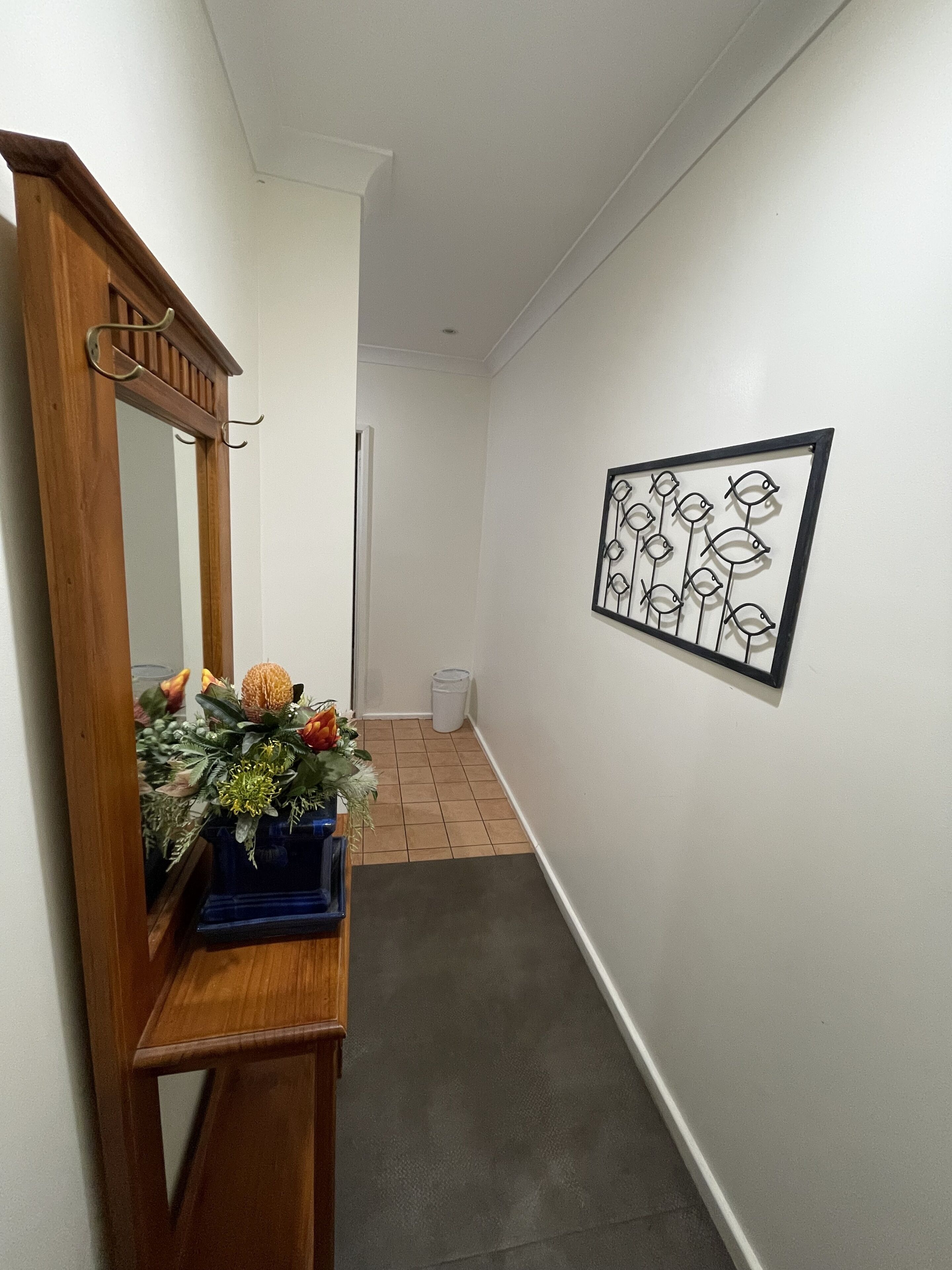A hallway with a wooden bench, a mirror, a framed artwork, and a trash can.
