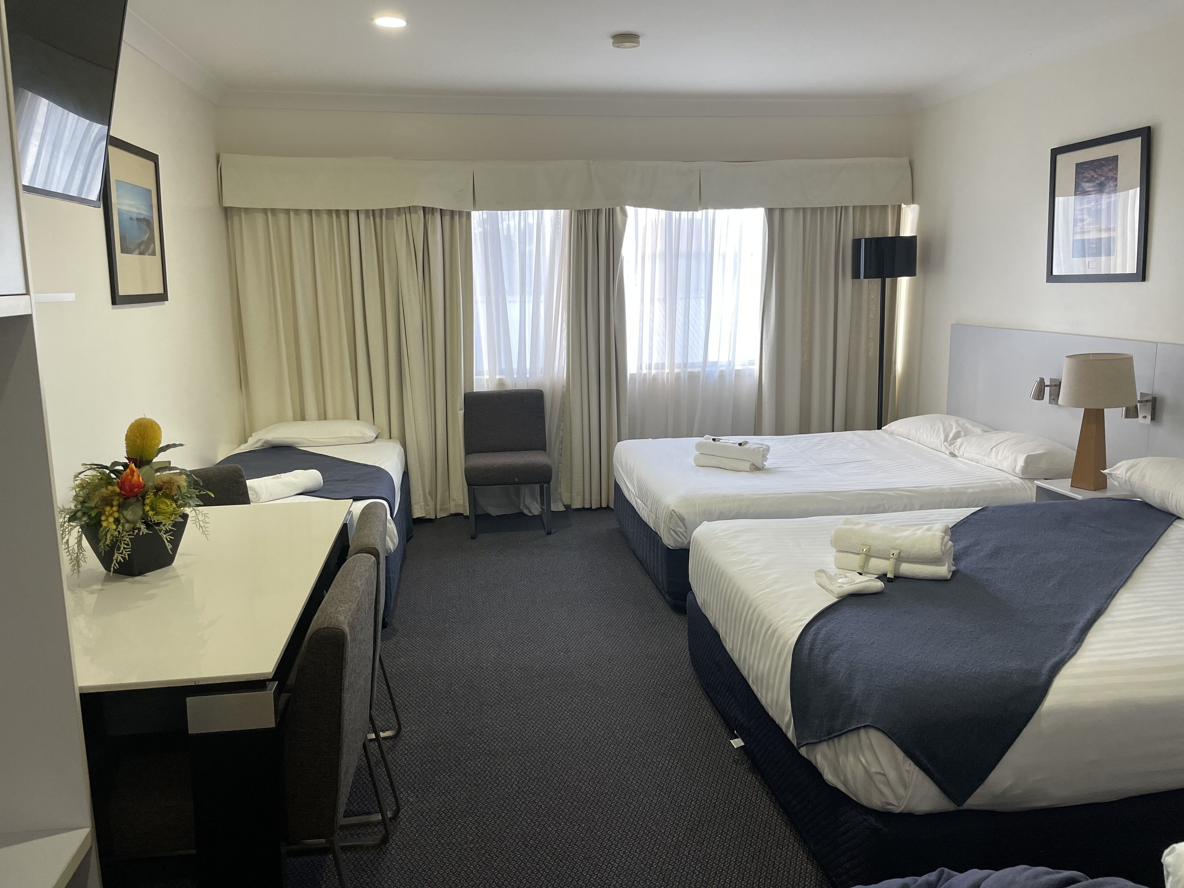 A hotel room with two beds, a desk, a chair, a TV, and a window with curtains.