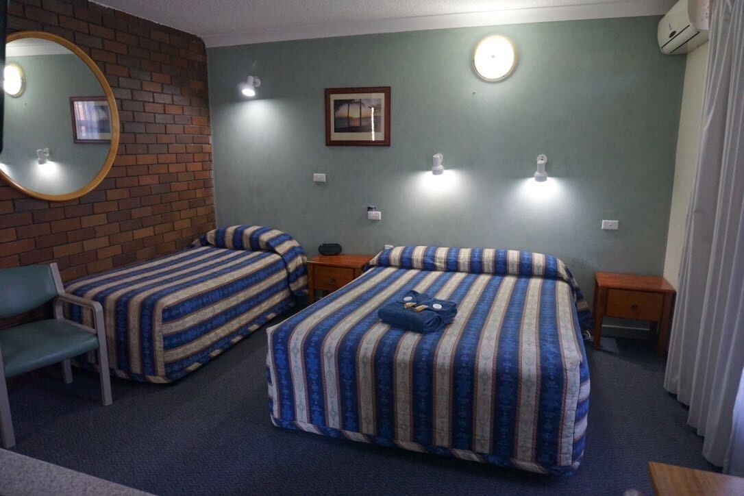 A hotel room with two beds, a mirror, a picture on the wall, and a small table.