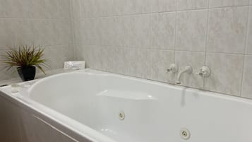 Een badkamer met een witte badkuip, een potplant en een wand betegeld met witte tegels.