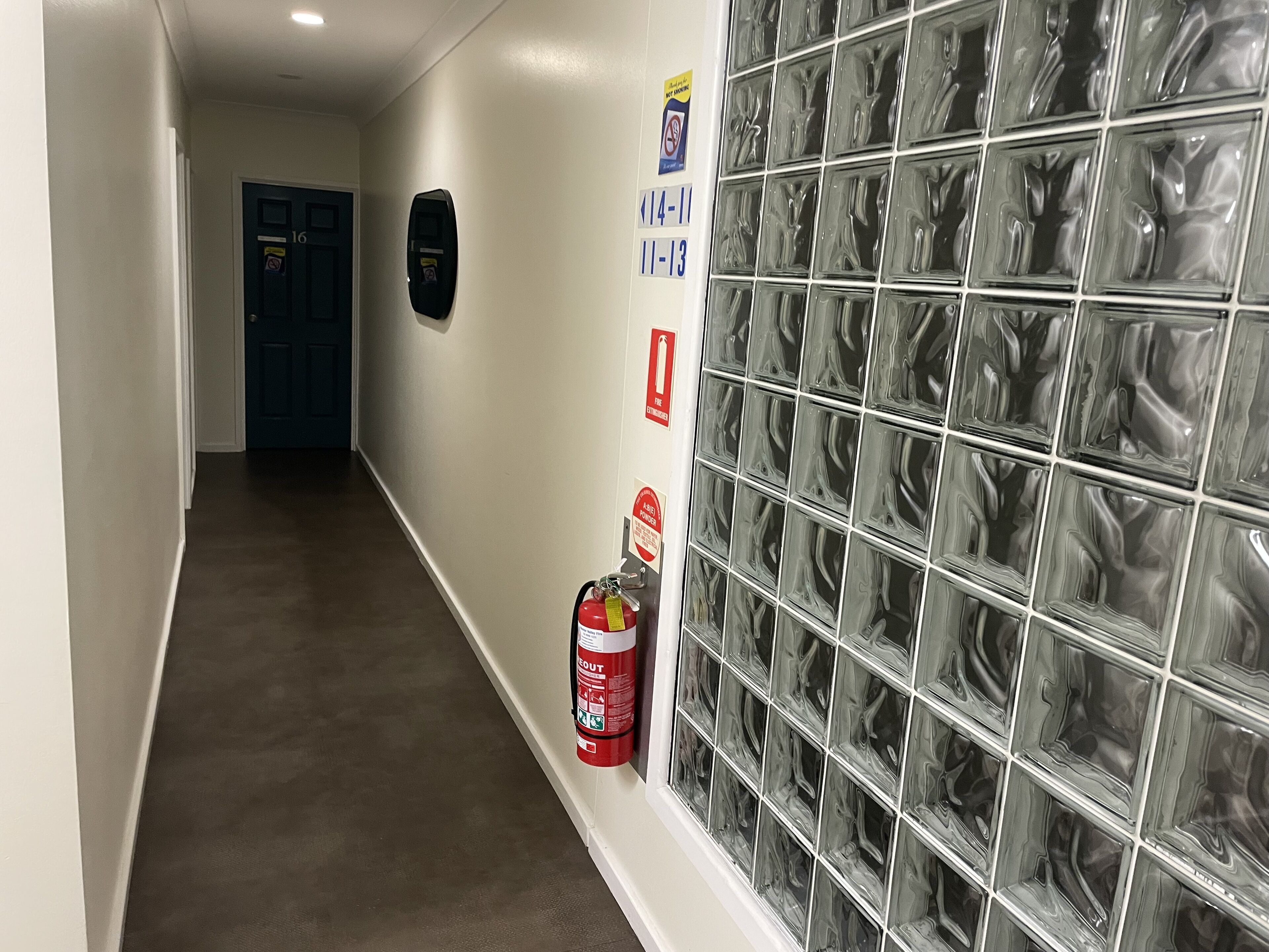 Un pasillo con un extintor, un detector de incendios y una puerta con números.