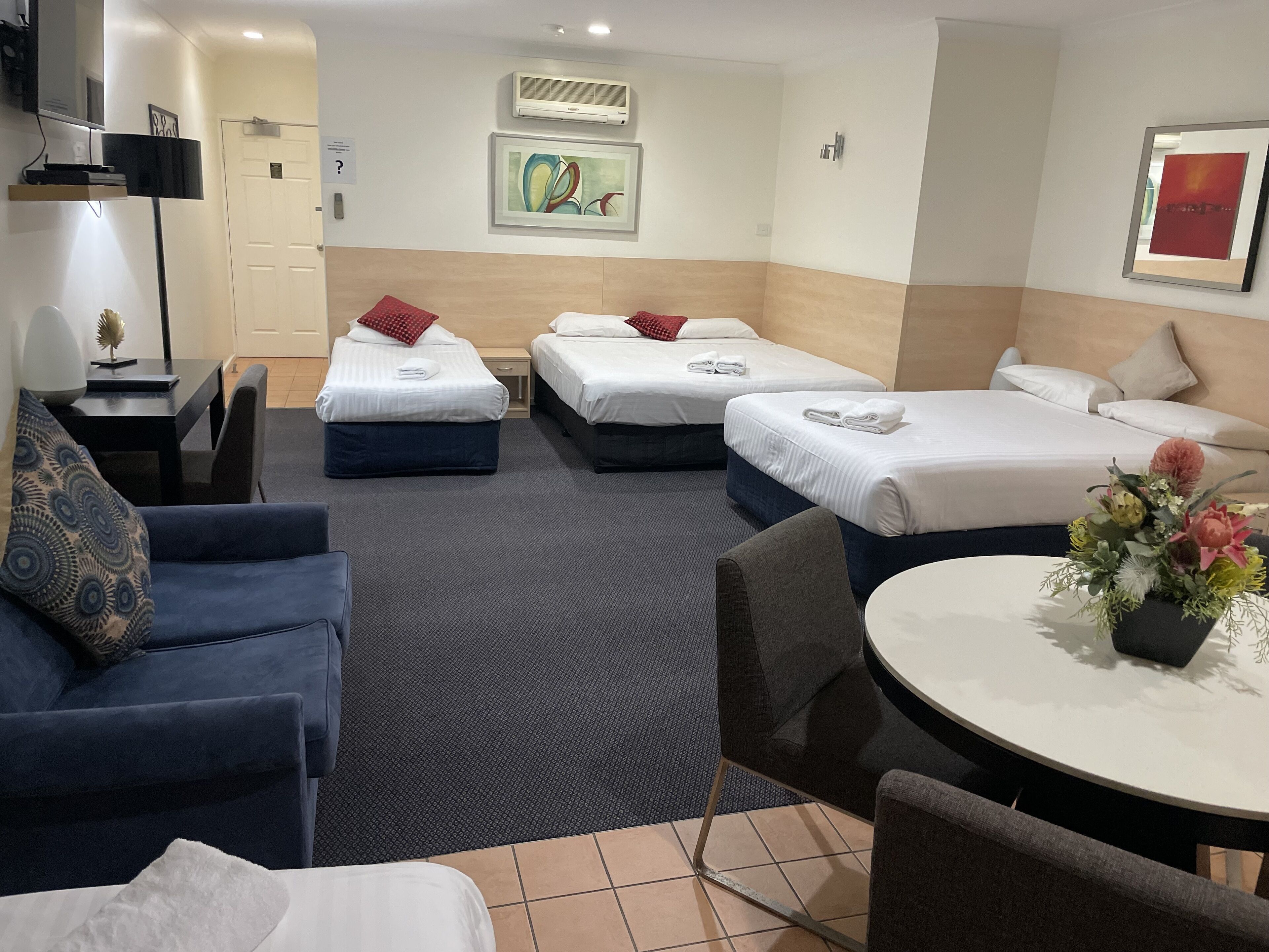 A hotel room with two single beds, a sofa, a dining table, and a TV.