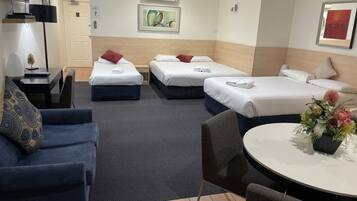 A hotel room with two single beds, a sofa, a dining table, and a TV.