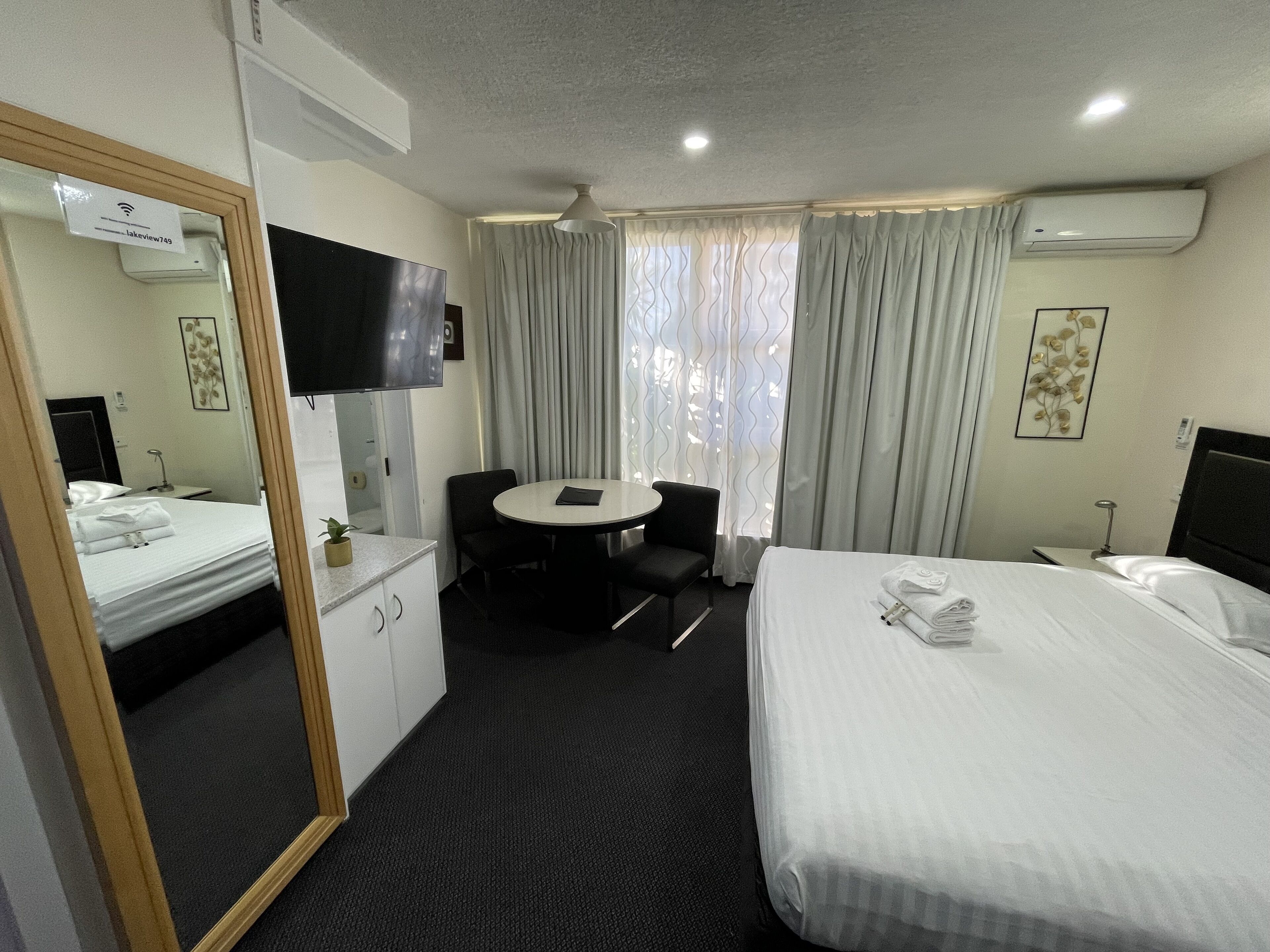 A hotel room with a bed, a desk, a chair, a TV, and a window with curtains.