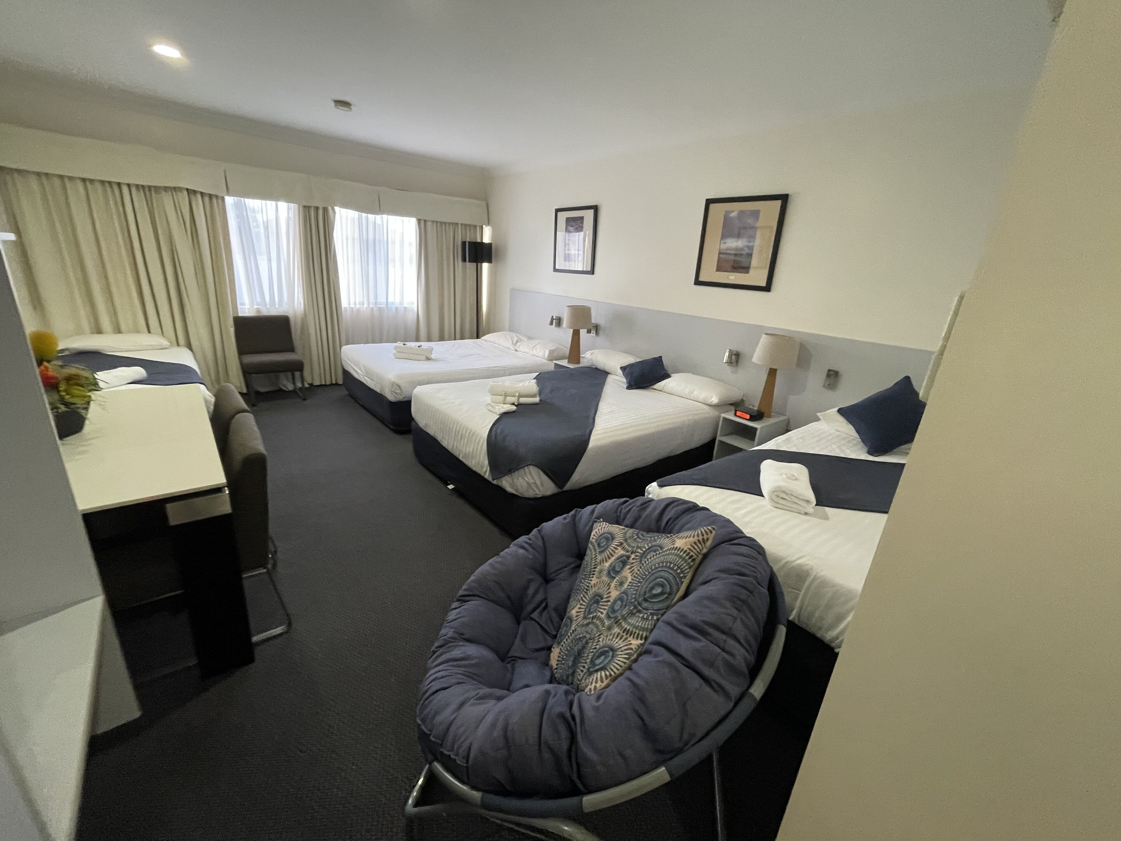 A hotel room with three beds, a desk, and a chair.