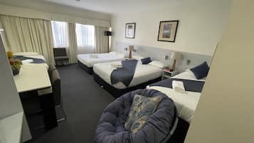 A hotel room with three beds, a desk, and a chair.