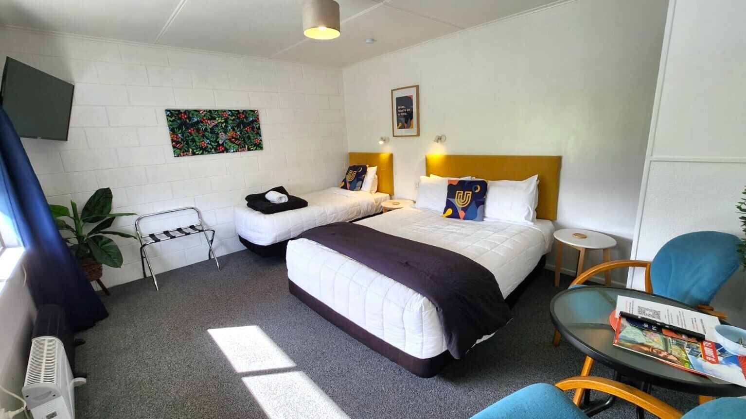 Ein Hotelzimmer mit zwei Betten, einem kleinen Tisch, einem Stuhl, einer Pflanze und einem Fernseher.