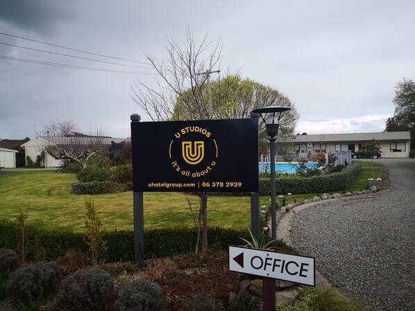 A sign for U Studios with a contact number and website, an office sign, and a pool area. - U Studios Masterton, SureStay Collection by BW (Masterton)