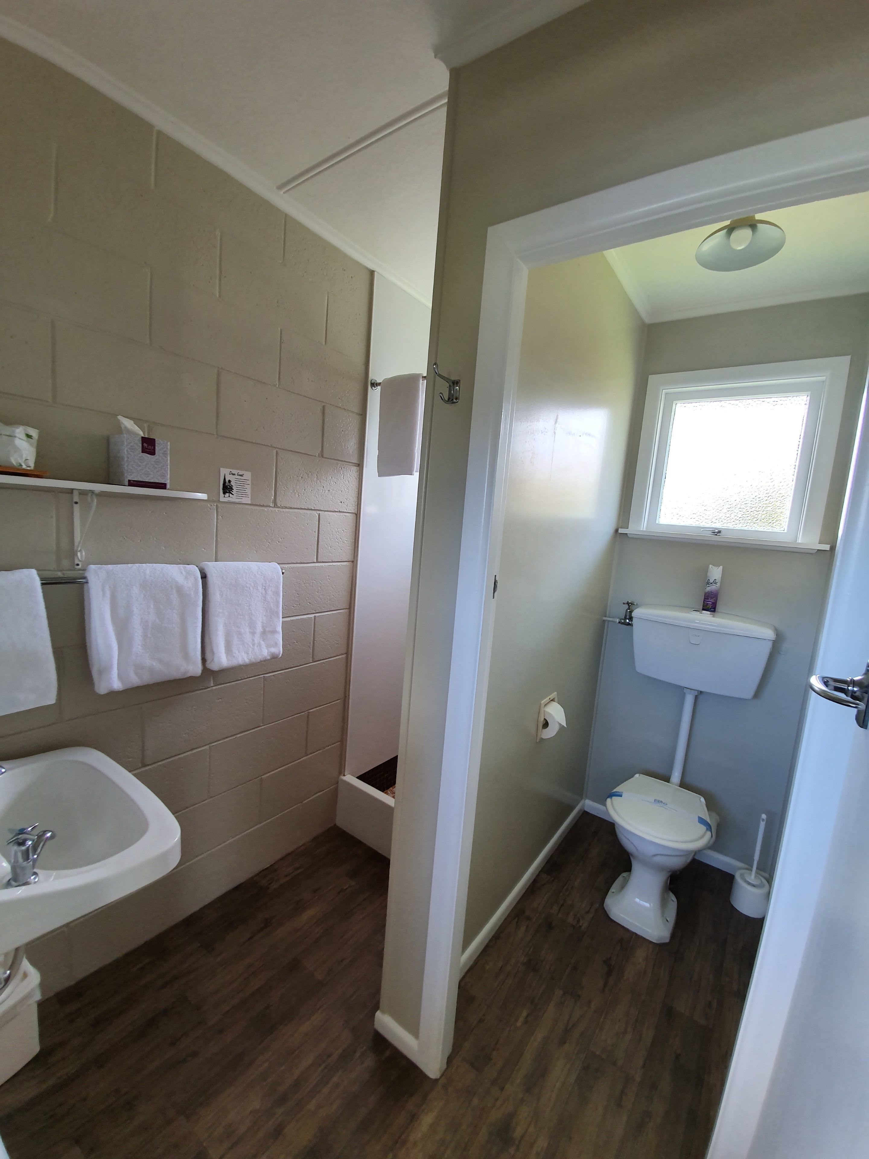 A bathroom with a sink, toilet, and shower. There are towels hanging on the wall and a window above the toilet.