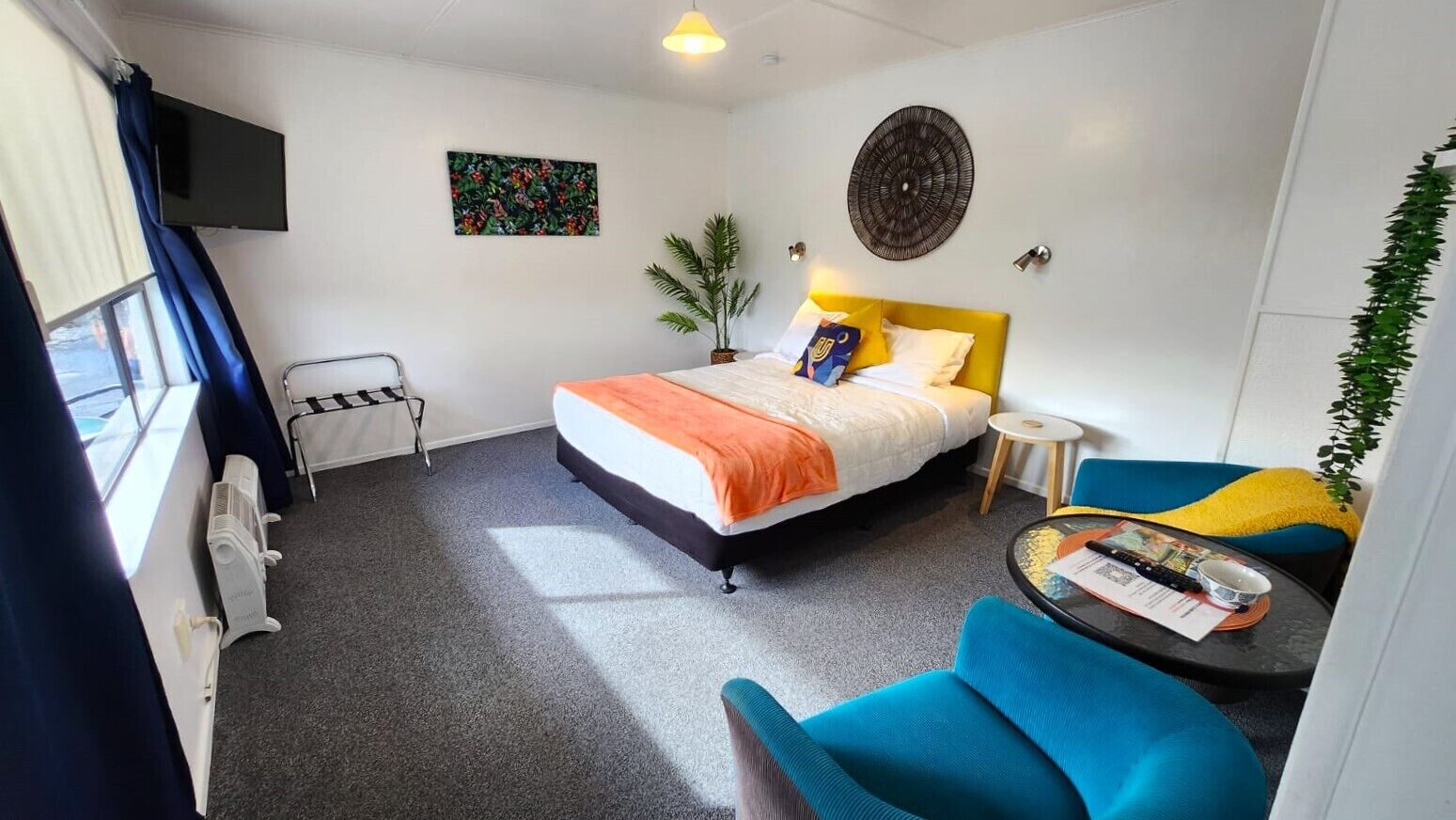 Une chambre d’hôtel avec un lit, une petite table, une chaise, un téléviseur et une fenêtre avec des rideaux.