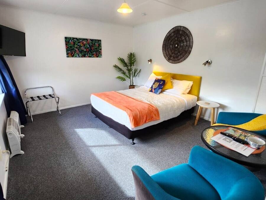 A hotel room with a bed, a small table, a chair, a TV, and a window with curtains.
