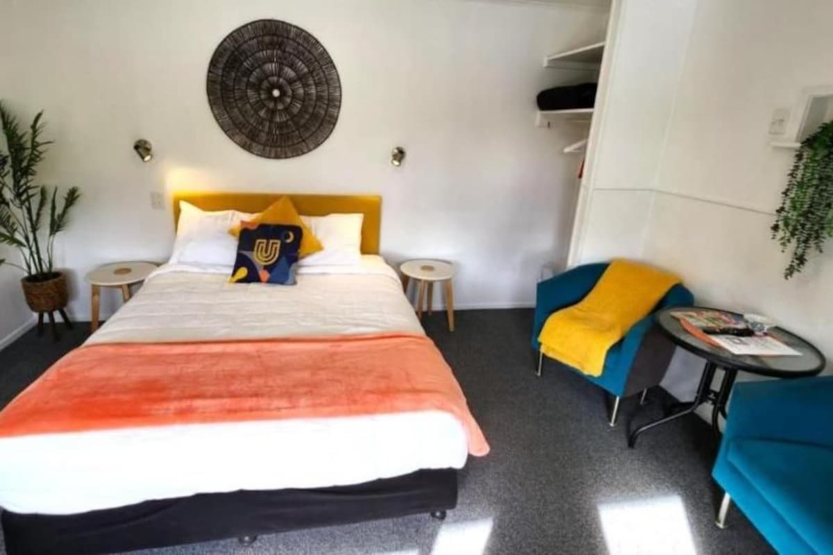 A hotel room with a bed, a small table, a chair, and a potted plant.